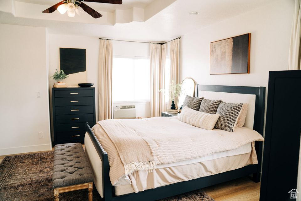 Bedroom featuring a wall mounted AC, wood finished floors, baseboards, and ceiling fan