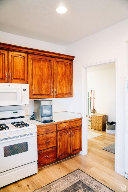 Kitchen with brown cabinets, white appliances, light wood finished floors, and light countertops