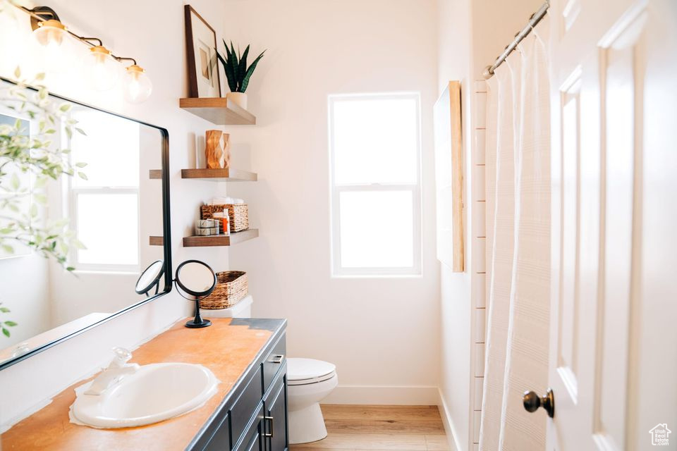 Full bath with toilet, wood finished floors, vanity, and a healthy amount of sunlight