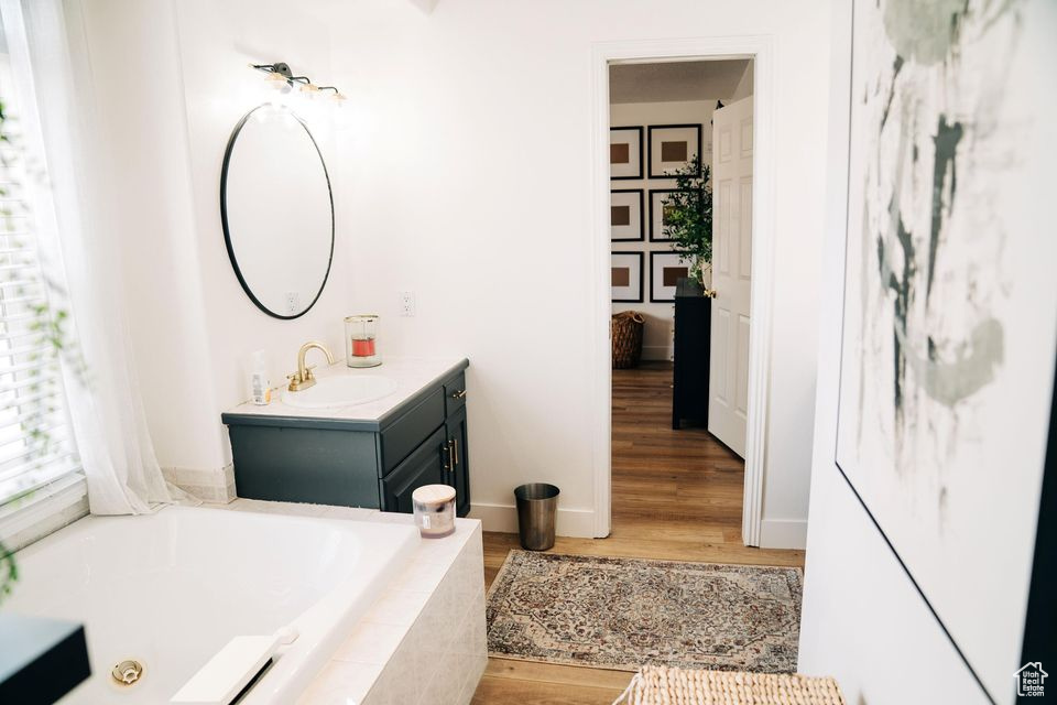 Bathroom featuring baseboards, a garden tub, vanity, and wood finished floors