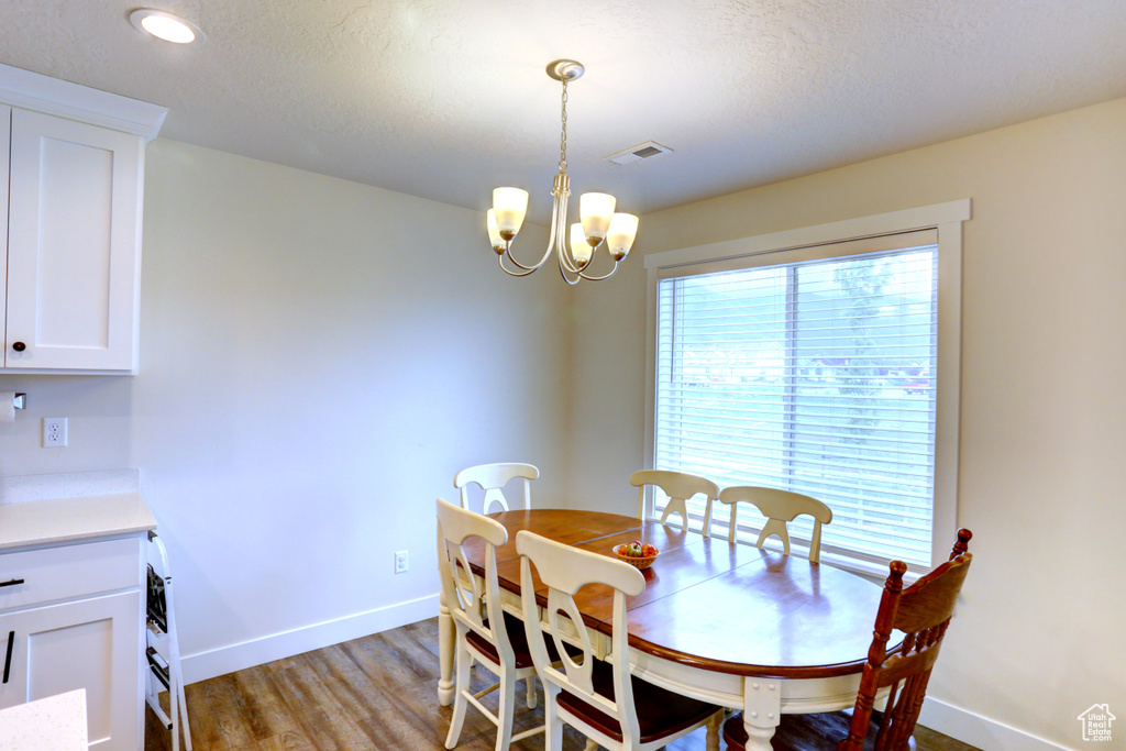 Dining space with a textured ceiling, light wood-type flooring, visible vents, a chandelier, and baseboards