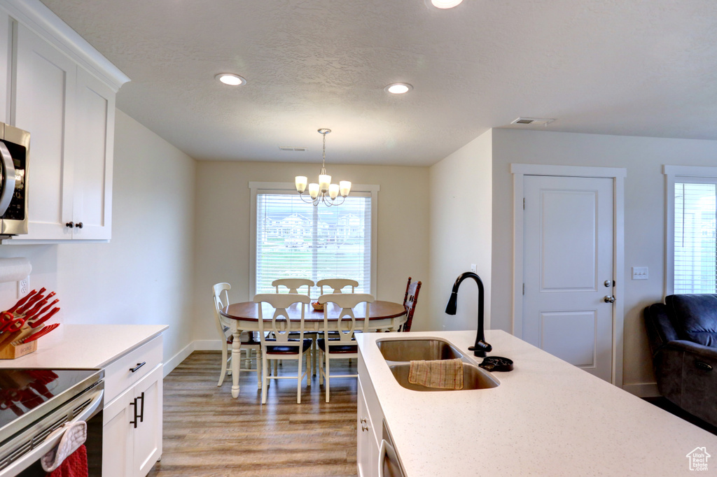 Kitchen featuring a notable chandelier, light wood-style flooring, a healthy amount of sunlight, a sink, and white cabinetry