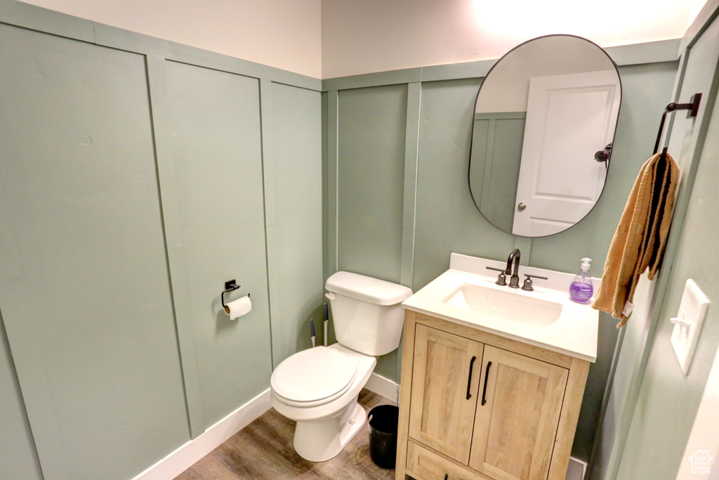Half bathroom with vanity, toilet, a decorative wall, and wood finished floors