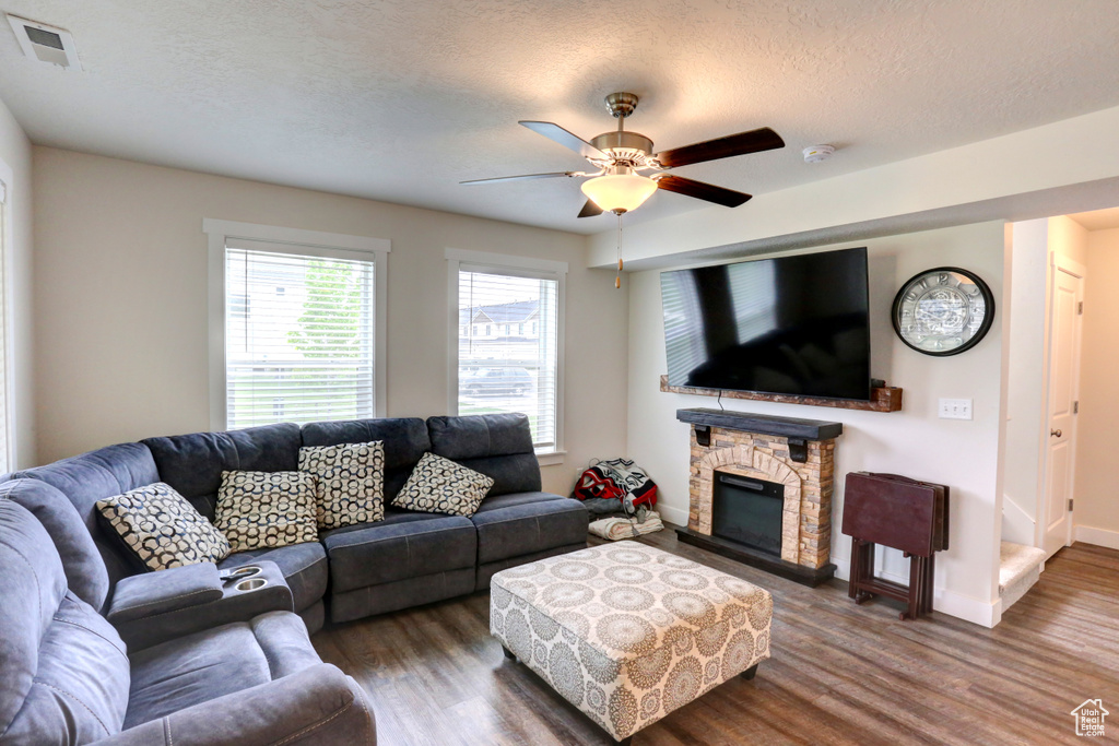 Living room with wood finished floors, a textured ceiling, visible vents, a ceiling fan, and a stone fireplace