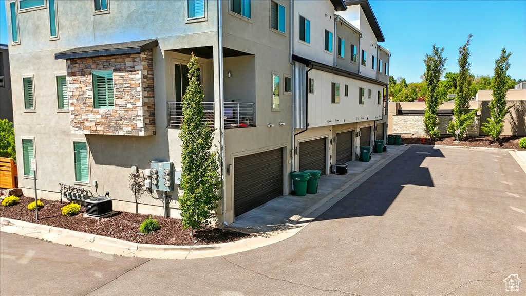 View of property exterior featuring central AC unit, stone siding, stucco siding, and a garage