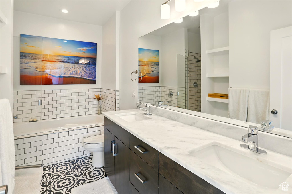 Full bath featuring a sink, tile patterned flooring, double vanity, and a relaxing tiled tub
