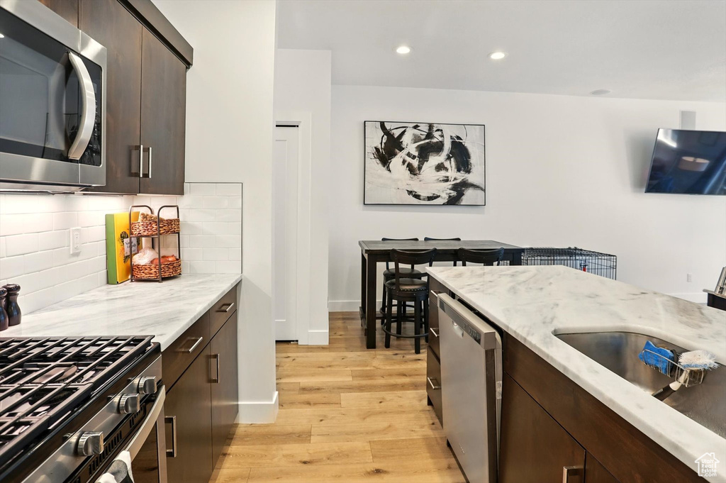 Kitchen with tasteful backsplash, light wood-type flooring, dark brown cabinets, and appliances with stainless steel finishes