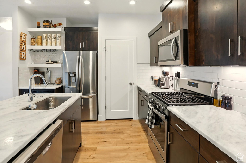 Kitchen featuring a sink, open shelves, light wood-type flooring, dark brown cabinets, and appliances with stainless steel finishes