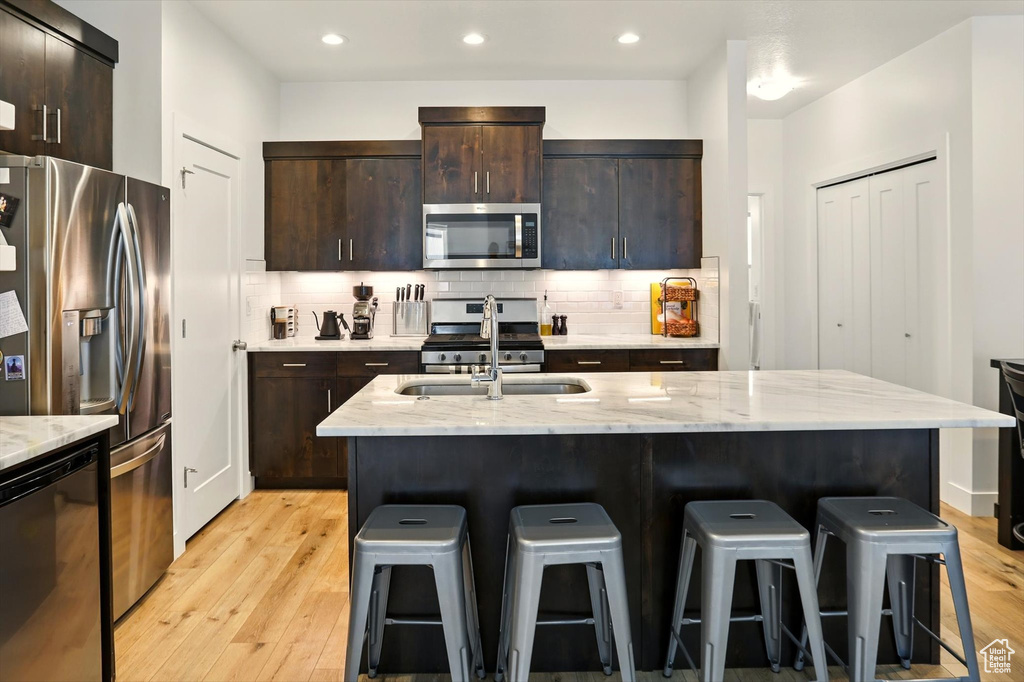 Kitchen featuring light wood-type flooring, appliances with stainless steel finishes, a breakfast bar area, and a sink