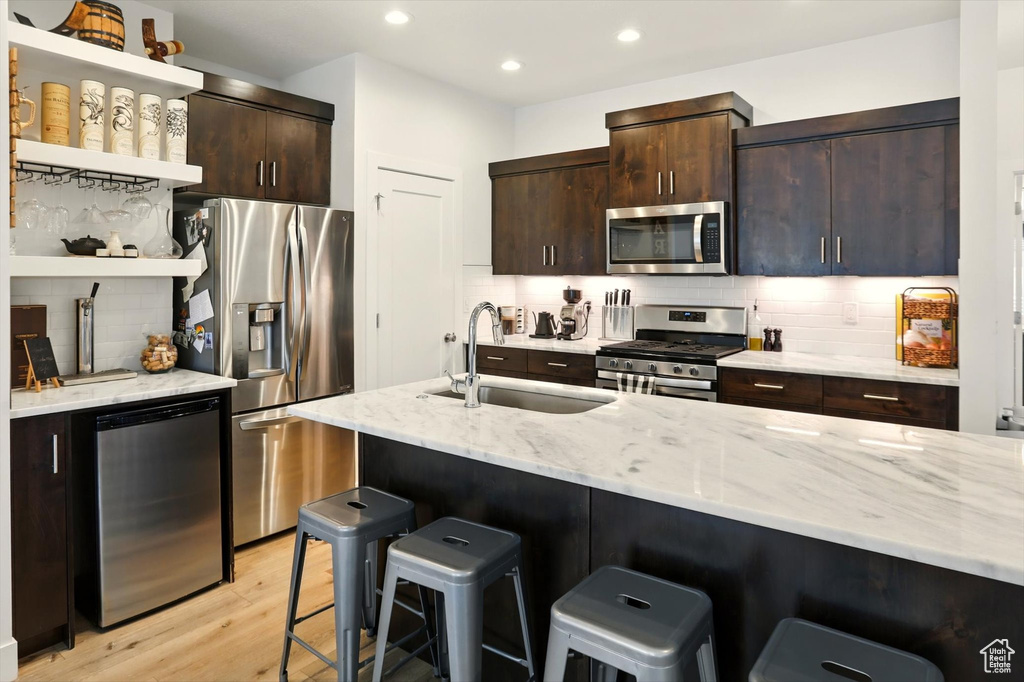 Kitchen with open shelves, appliances with stainless steel finishes, a breakfast bar, and a sink