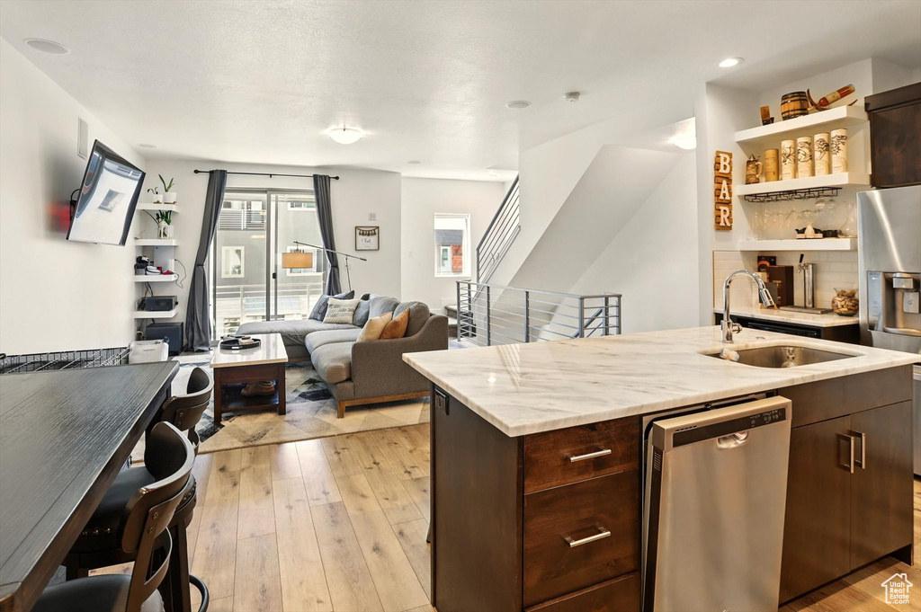 Kitchen featuring a sink, a kitchen island with sink, dark brown cabinetry, light wood-style flooring, and appliances with stainless steel finishes