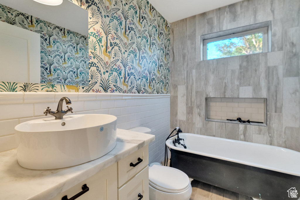 Full bath featuring tile walls, wallpapered walls, toilet, a soaking tub, and vanity