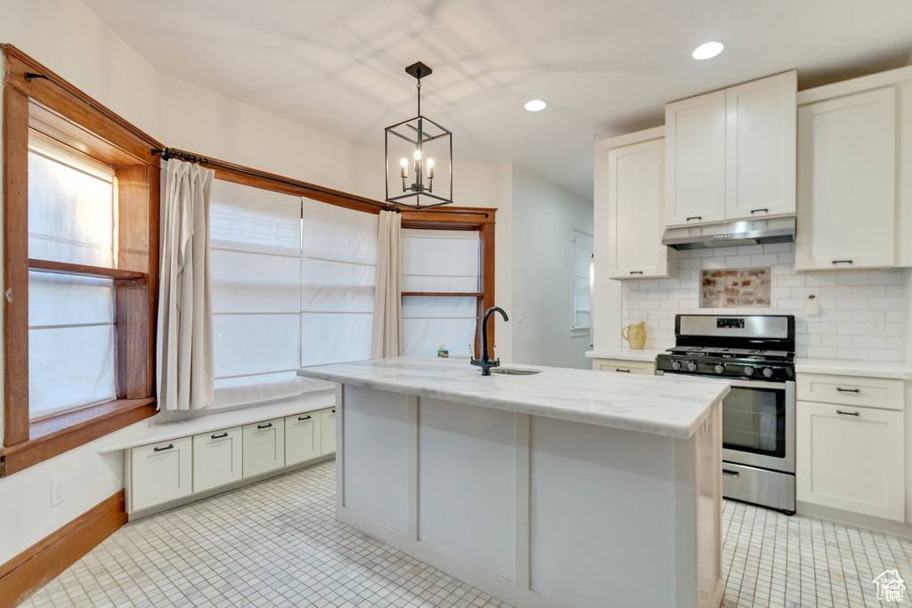 Kitchen with under cabinet range hood, stainless steel range with gas stovetop, a sink, and a healthy amount of sunlight