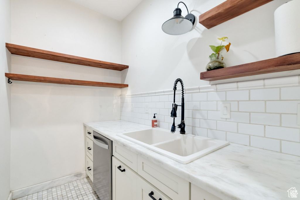 Kitchen featuring dishwasher, a sink, open shelves, decorative backsplash, and white cabinets