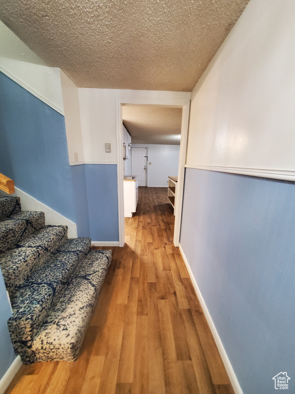 Corridor with a textured ceiling, stairway, and wood finished floors