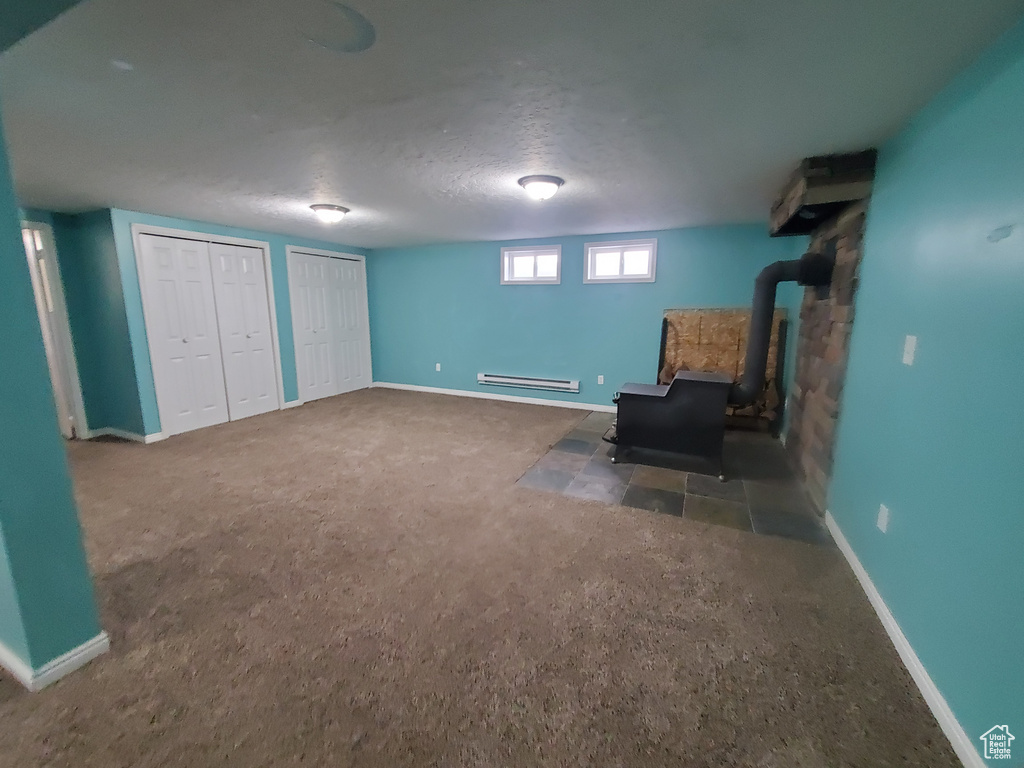 Unfurnished room featuring carpet floors, a textured ceiling, baseboards, a baseboard heating unit, and a wood stove