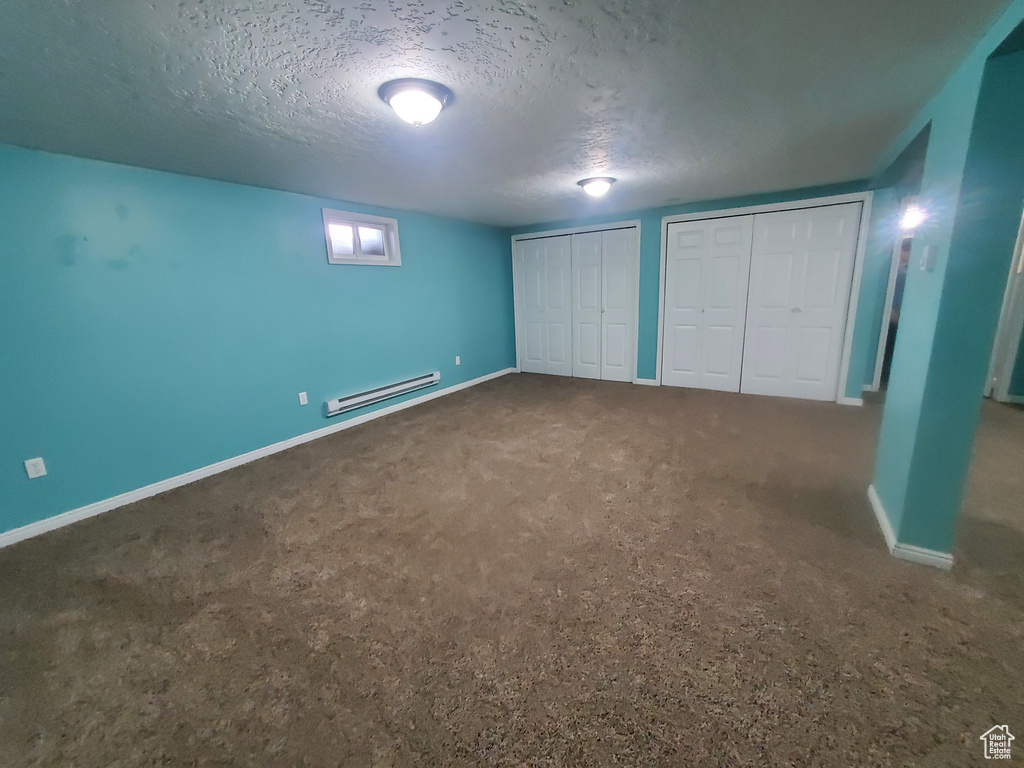 Unfurnished bedroom featuring a baseboard radiator, carpet, a textured ceiling, baseboards, and multiple closets