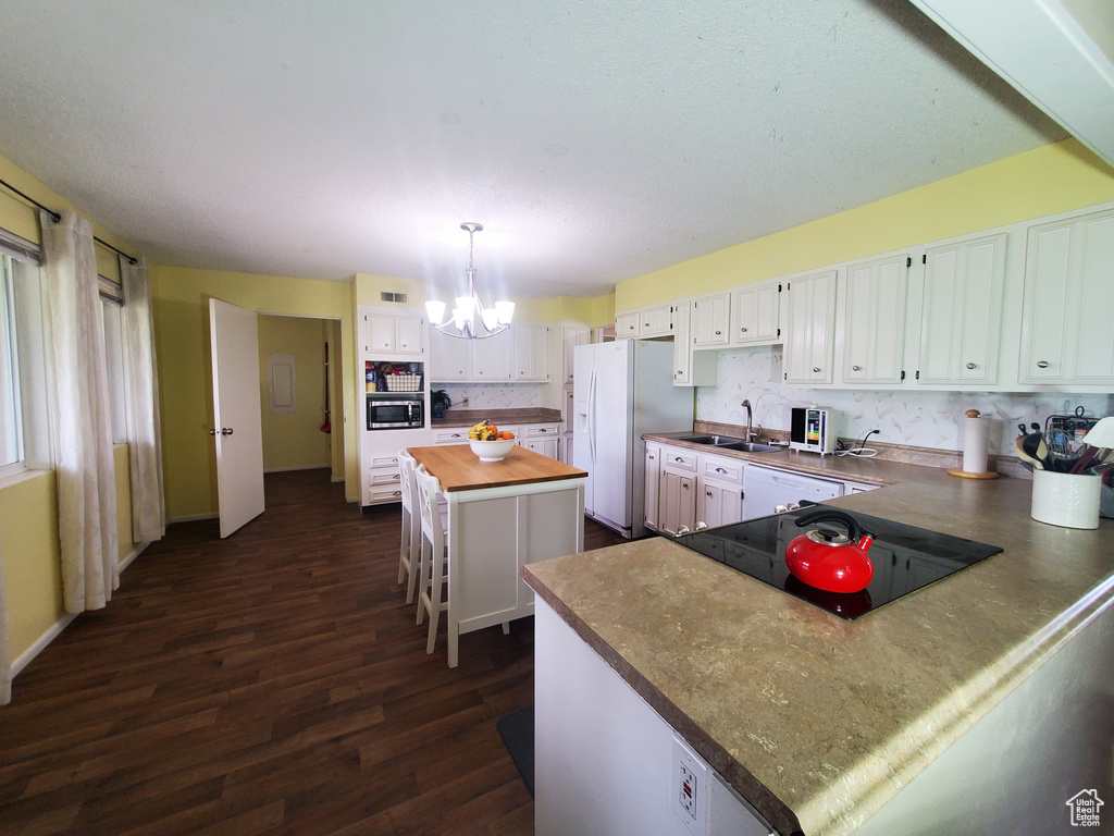 Kitchen featuring white fridge with ice dispenser, a chandelier, butcher block countertops, dark wood finished floors, and cooktop