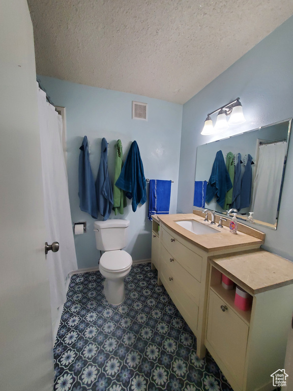 Bathroom featuring a textured ceiling, toilet, baseboards, visible vents, and vanity
