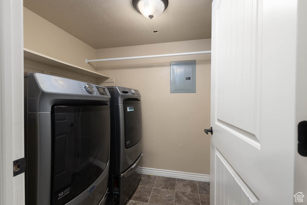 Clothes washing area with washing machine and dryer, a textured ceiling, baseboards, electric panel, and laundry area