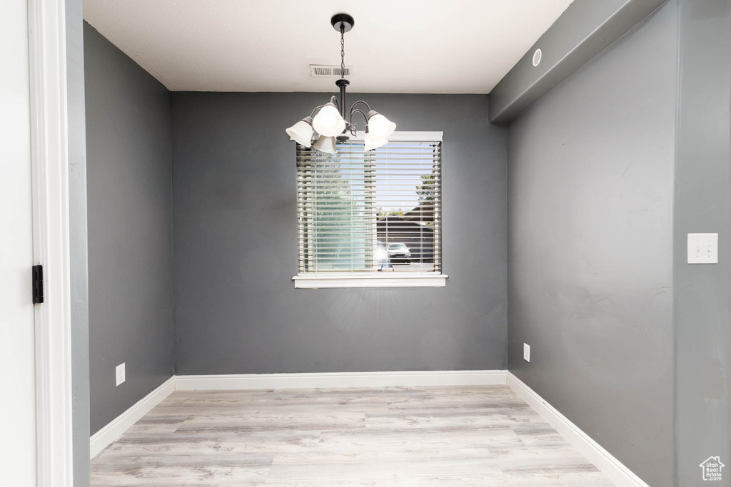 Unfurnished room with a chandelier, light wood-style flooring, baseboards, and visible vents