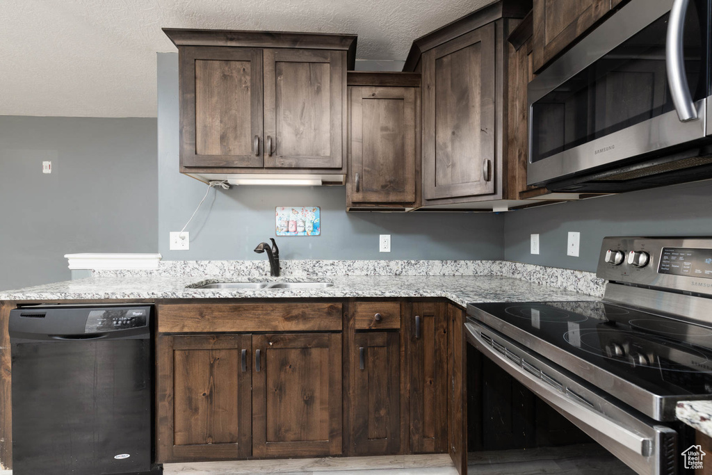 Kitchen featuring a sink, stainless steel appliances, dark brown cabinetry, a textured ceiling, and light stone counters