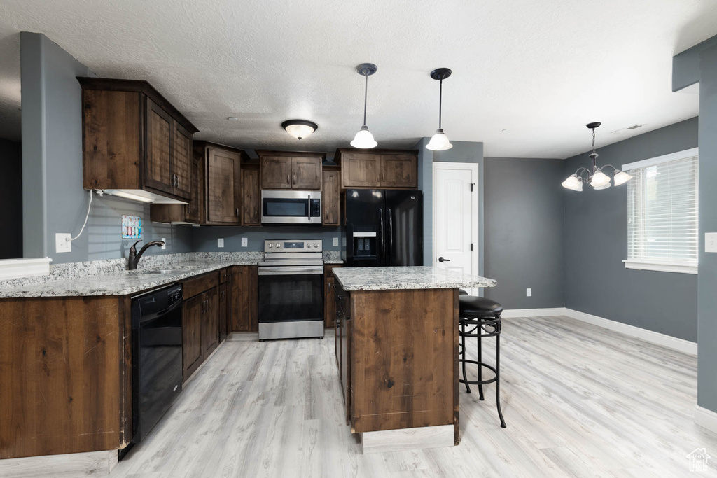 Kitchen with baseboards, black appliances, light wood finished floors, and a kitchen bar