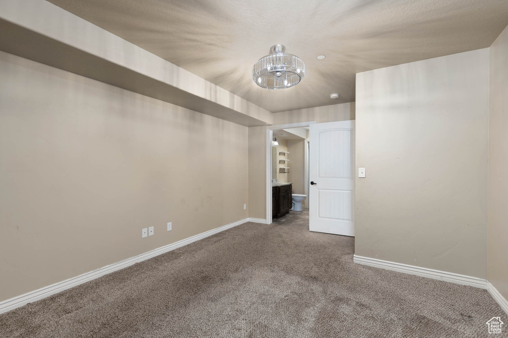 Spare room featuring an inviting chandelier, carpet, and baseboards