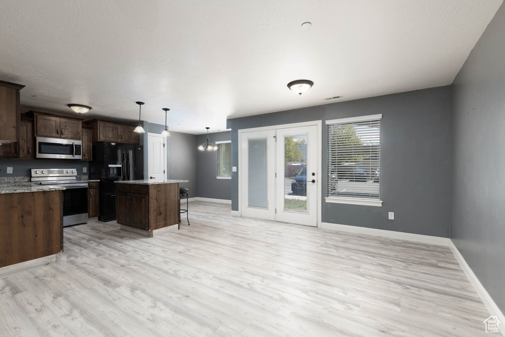 Kitchen with appliances with stainless steel finishes, a center island, baseboards, a kitchen bar, and light wood-type flooring