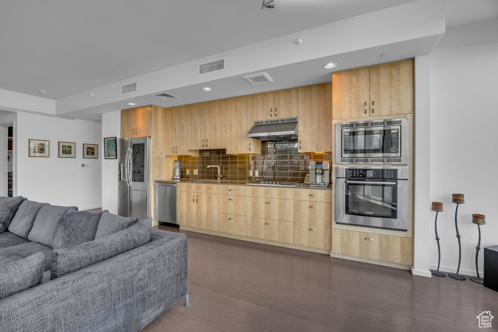 Kitchen with light brown cabinets, under cabinet range hood, visible vents, open floor plan, and stainless steel appliances