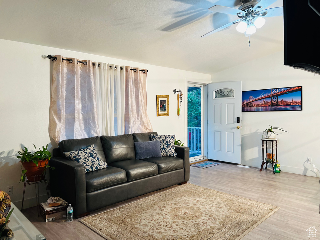 Living area with light wood-style floors, vaulted ceiling, baseboards, and ceiling fan
