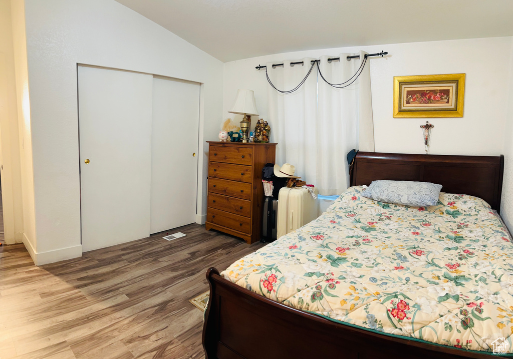 Bedroom with lofted ceiling, a closet, visible vents, and wood finished floors