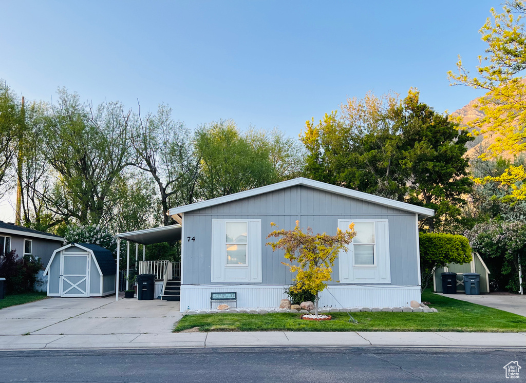 View of property exterior with a lawn, concrete driveway, an outdoor structure, and a storage unit