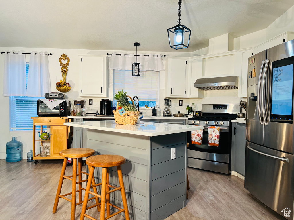 Kitchen with exhaust hood, a kitchen island, light wood-style floors, light countertops, and appliances with stainless steel finishes