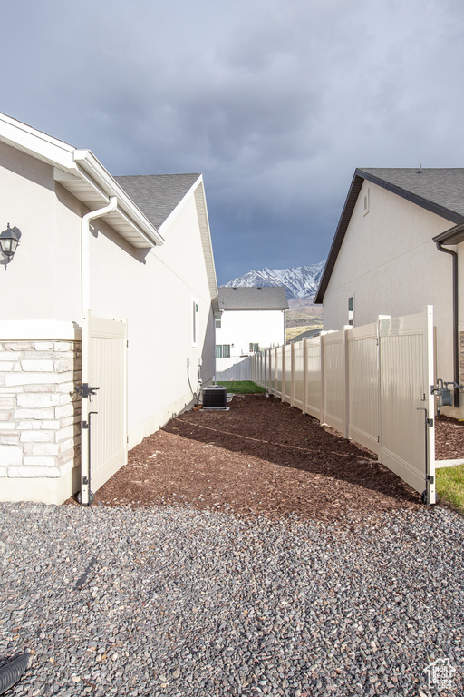 View of home\'s exterior with a mountain view, central AC, stucco siding, fence, and roof with shingles