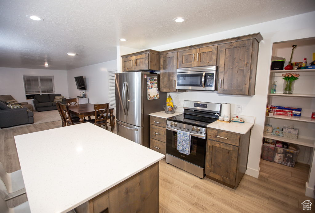 Kitchen featuring light wood-style flooring, a textured ceiling, light countertops, appliances with stainless steel finishes, and recessed lighting