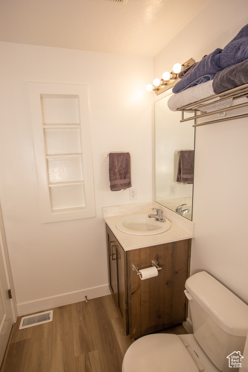 Bathroom with toilet, vanity, visible vents, and wood finished floors