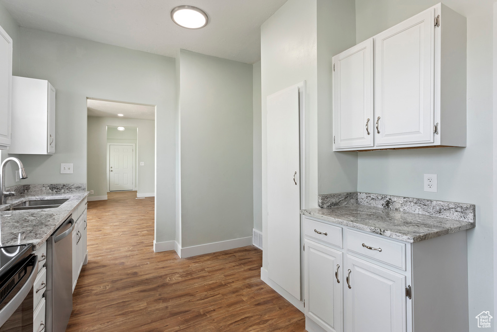 Kitchen with dark wood-style flooring, stainless steel dishwasher, a sink, baseboards, and white cabinetry