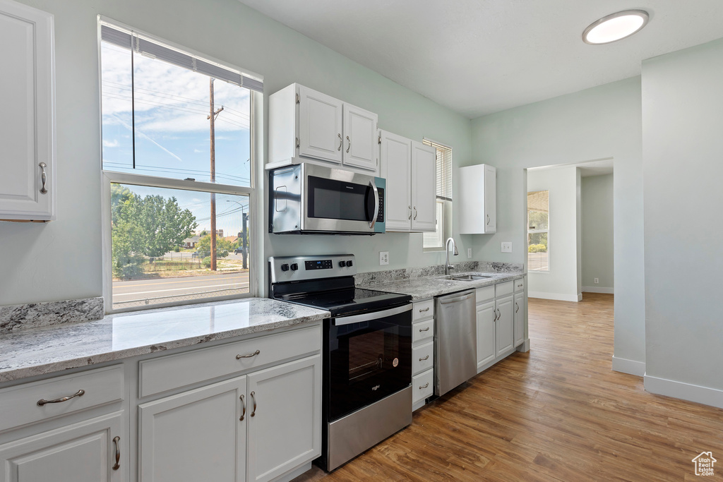 Kitchen with white cabinets, light stone countertops, appliances with stainless steel finishes, a sink, and light wood-style flooring