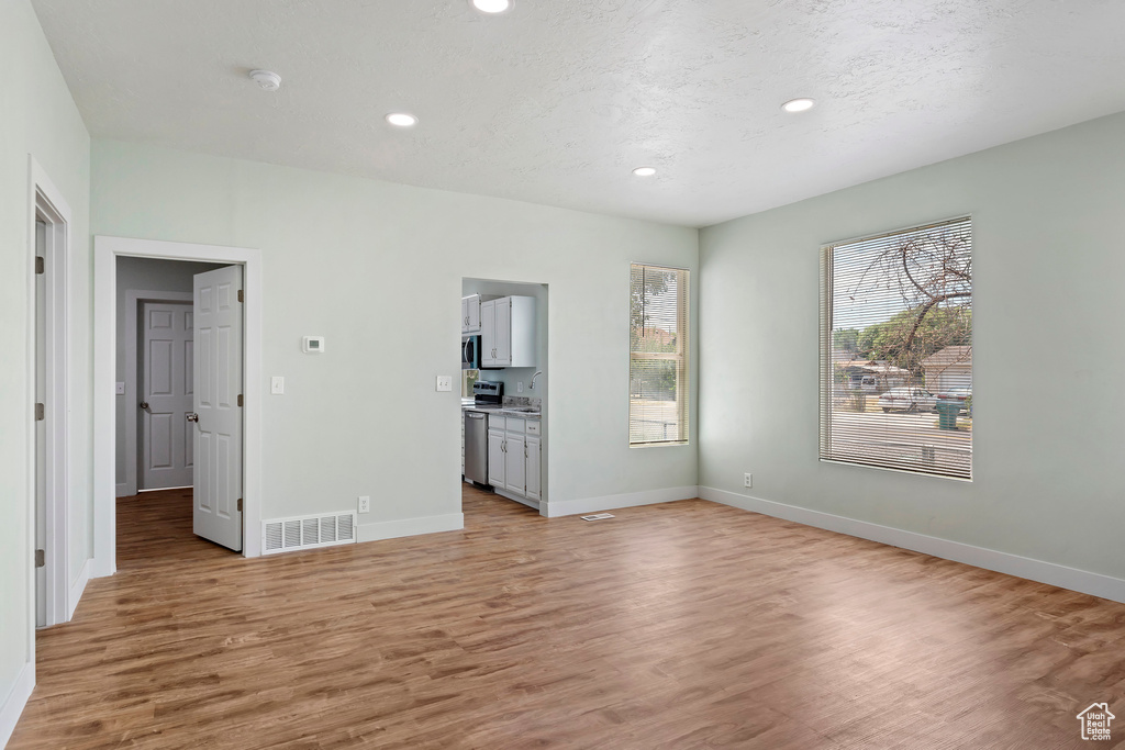 Unfurnished living room with light wood-style floors, baseboards, recessed lighting, and visible vents