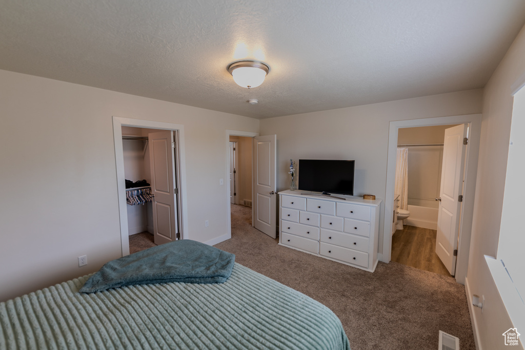 Carpeted bedroom with a closet, visible vents, baseboards, ensuite bath, and a spacious closet
