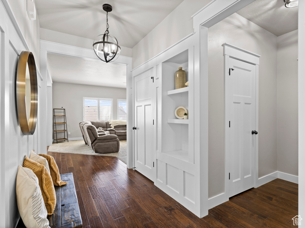 Hall with dark wood-style flooring, baseboards, a notable chandelier, and built in shelves
