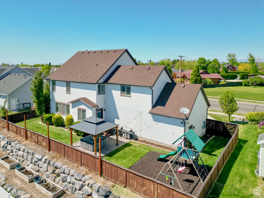 Back of house featuring a playground, stucco siding, a shingled roof, a gazebo, and a fenced backyard