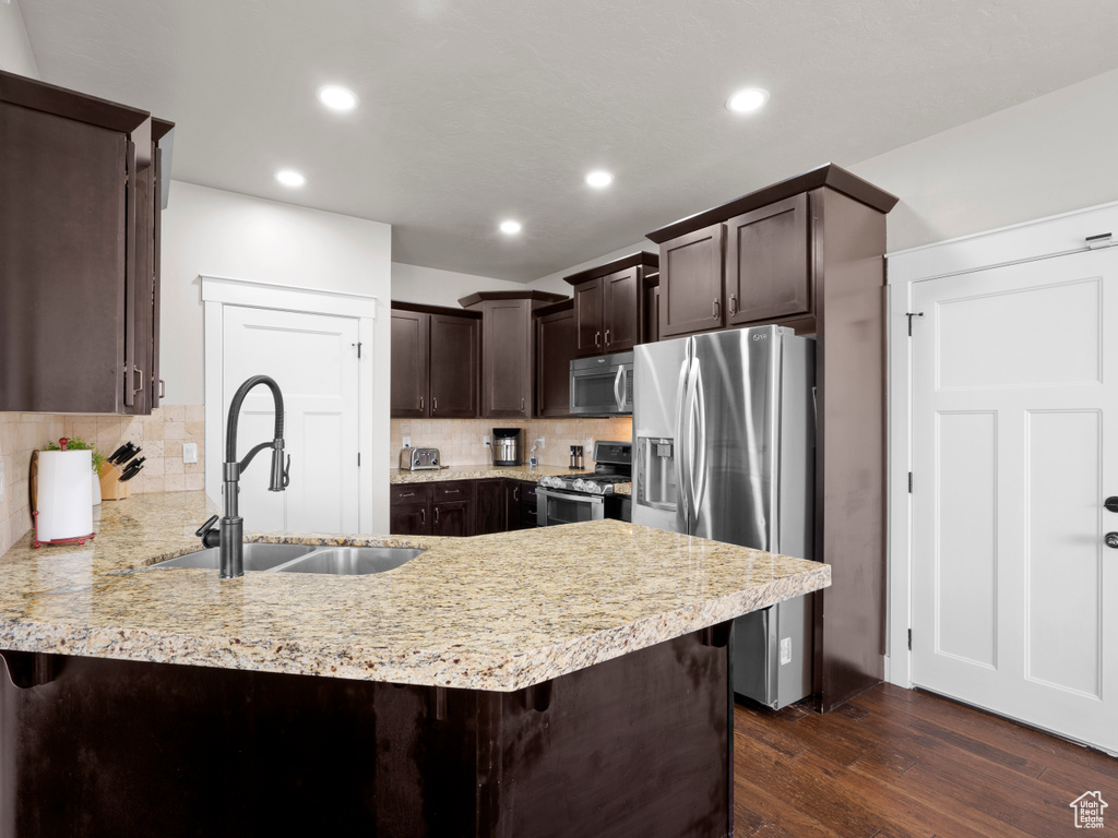 Kitchen featuring a peninsula, dark brown cabinets, a sink, backsplash, and appliances with stainless steel finishes