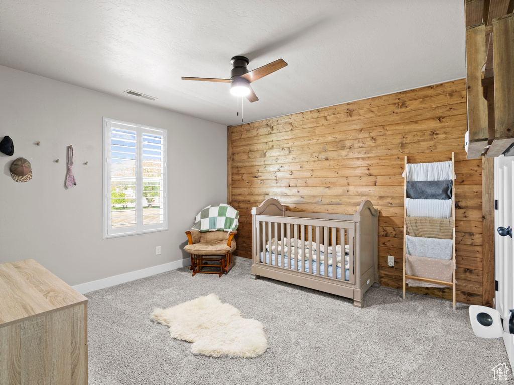 Bedroom with baseboards, carpet flooring, visible vents, wood walls, and a crib