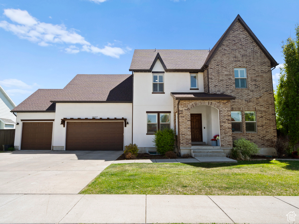 View of front facade featuring a garage, stucco siding, a front yard, brick siding, and driveway