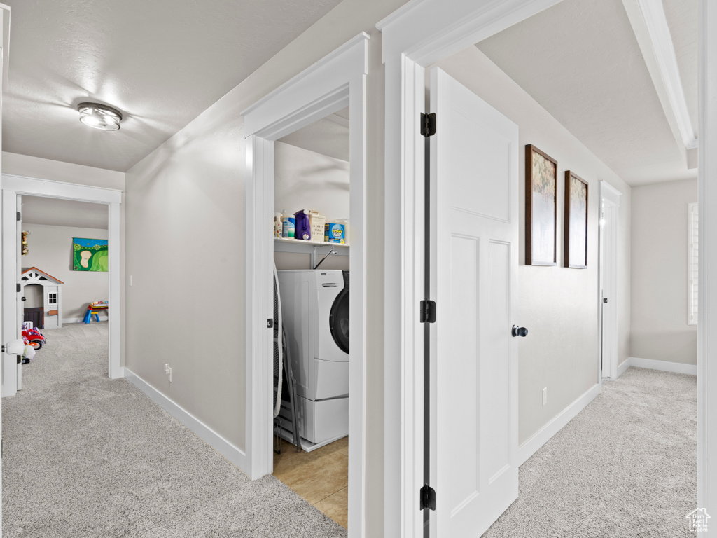 Hall with light colored carpet, washer / dryer, and baseboards