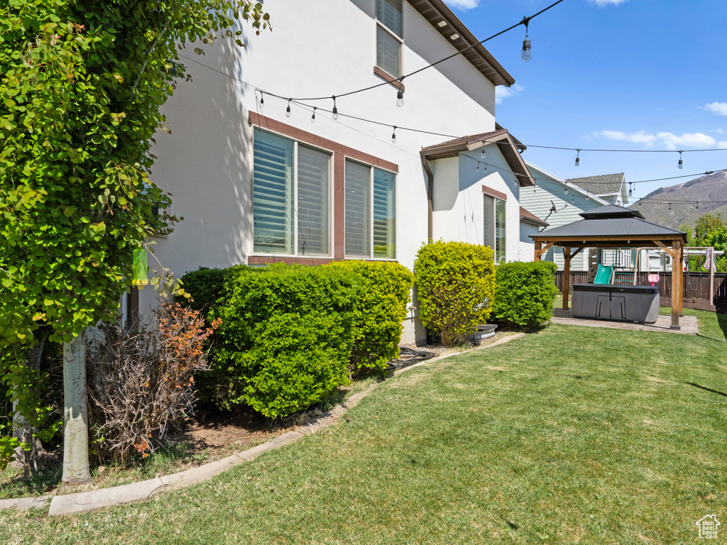 Rear view of property featuring a hot tub, stucco siding, a lawn, and a gazebo