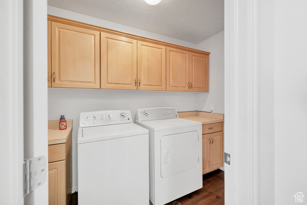 Washroom featuring dark wood finished floors, washer and dryer, and cabinet space