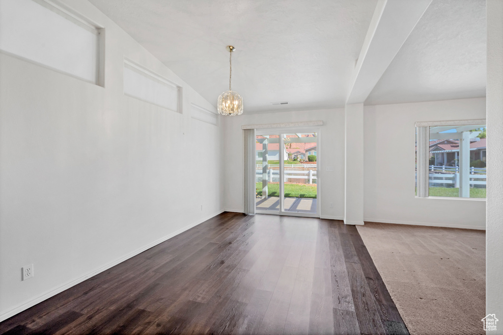 Unfurnished dining area with dark wood-style flooring, a notable chandelier, a healthy amount of sunlight, and vaulted ceiling